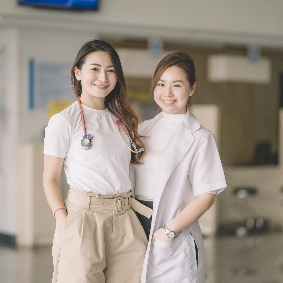 Duas profissionais de saúde sorridentes em ambiente clínico, uma delas com estetoscópio.